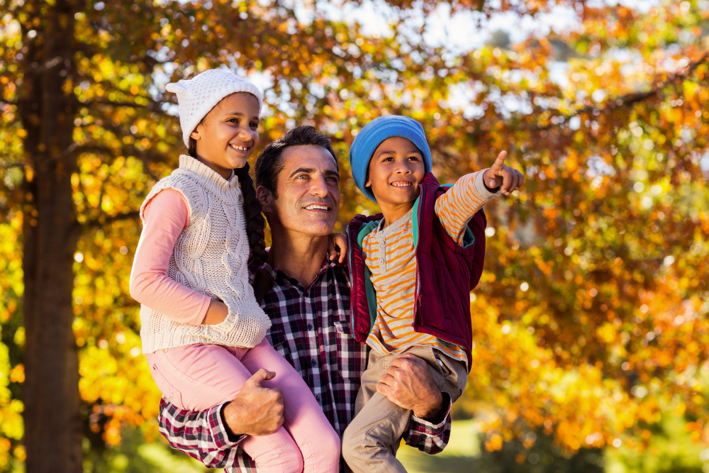 A young boy and girl on a mans shoulders while the boy points at something