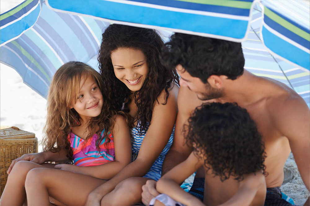 A family laughing under an umbrella on the beach